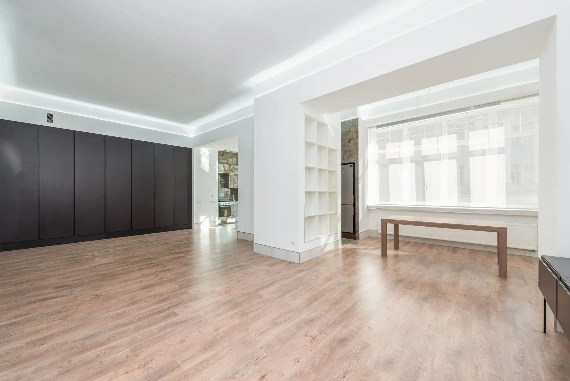 A bright open room with a pale oak floor running the length of it, freshly cleaned and catching the light from a tall window